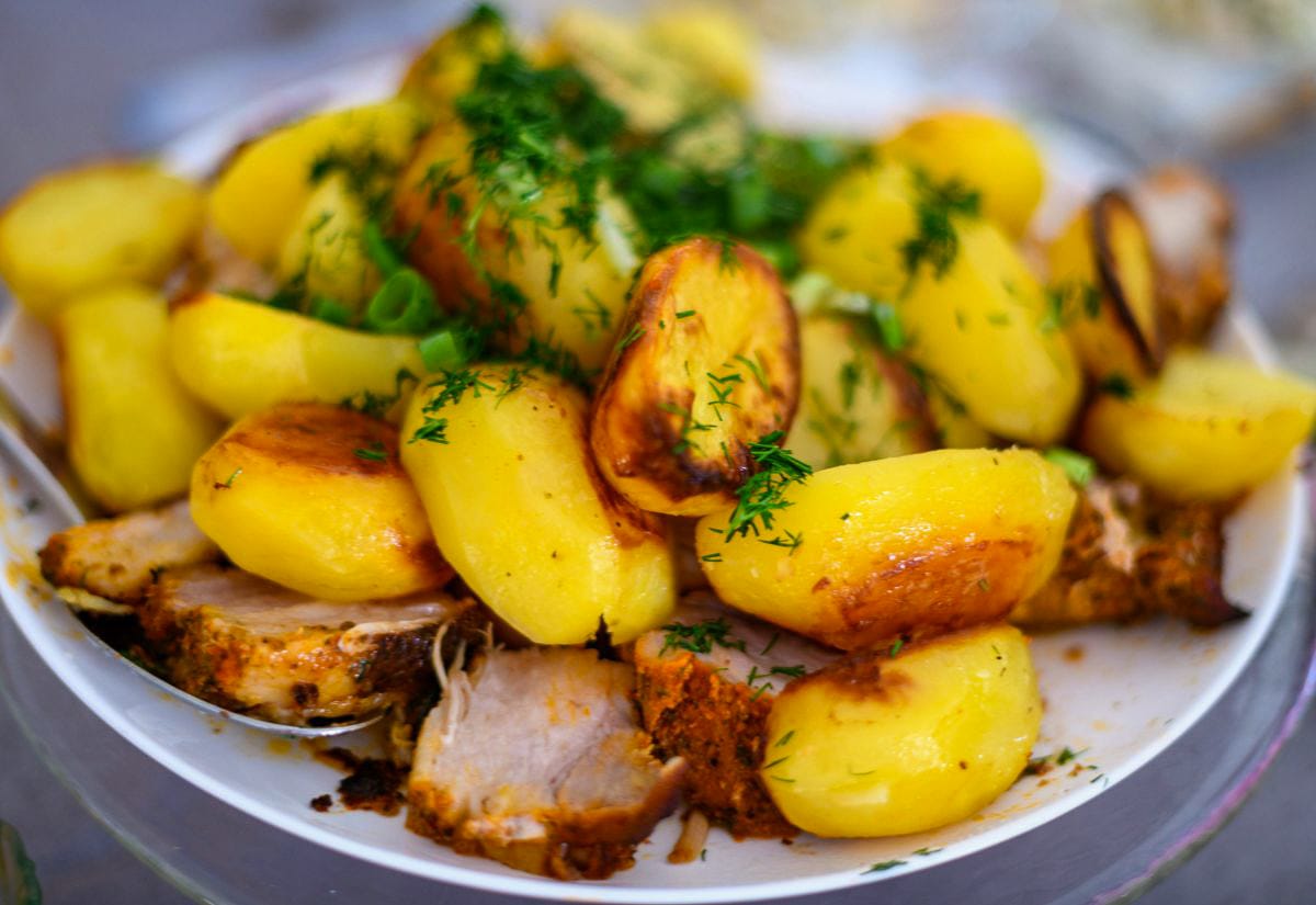 Plated ham slices topped with roasted potatoes and fresh herbs, served as a simple, hearty dinner.