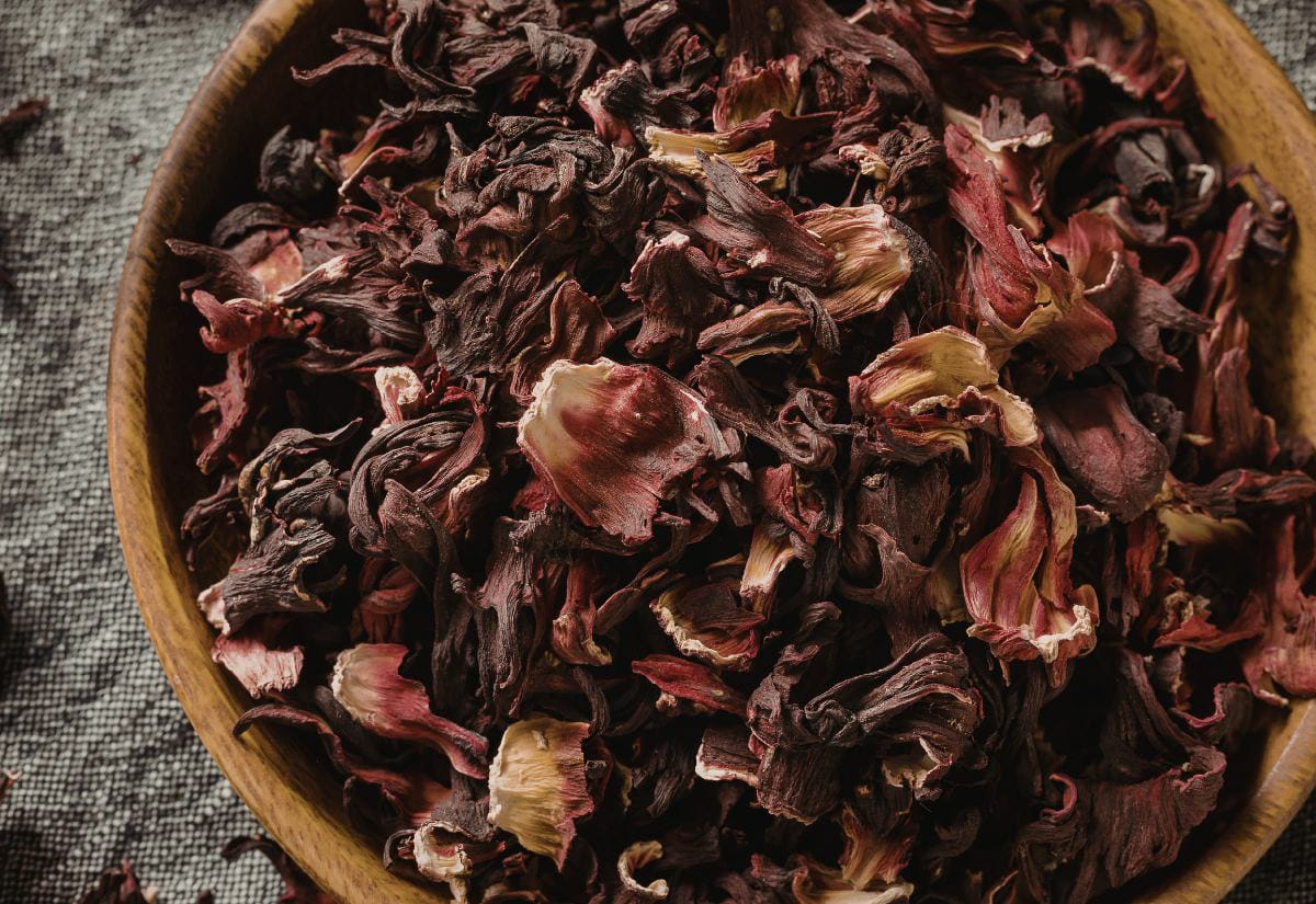 Bowl filled with deep red dried hibiscus petals, showing curled, textured pieces used for making tart herbal tea.